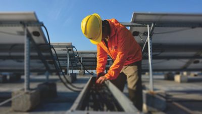 Technician installing cable management and balance-of-system components on a rooftop array